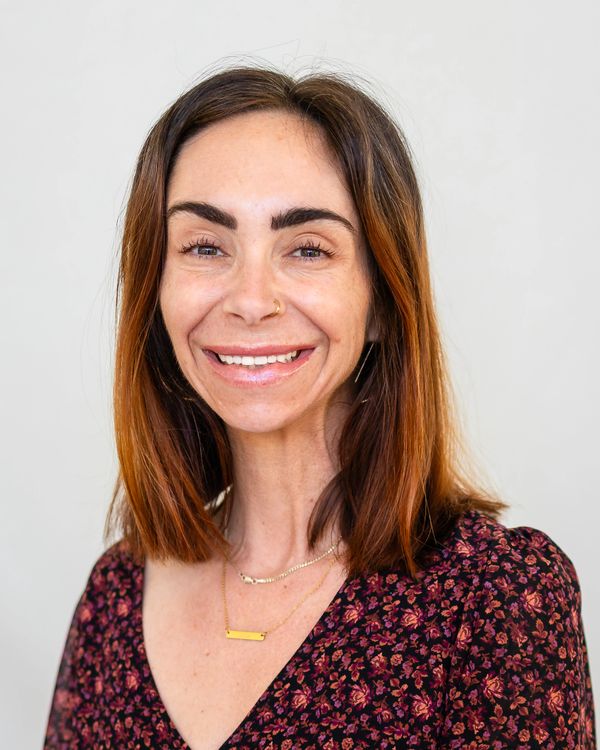 Smiling woman with shoulder-length brown hair and floral dress.