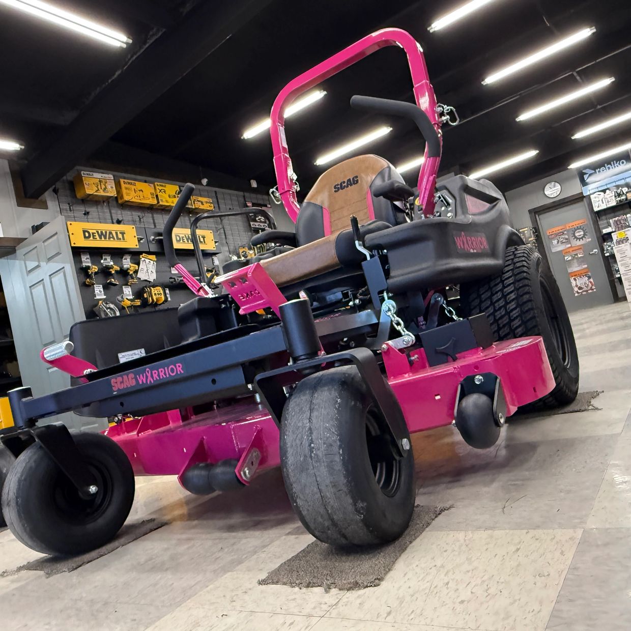 Bright pink Scag Warrior zero-turn lawn mower in a workshop.