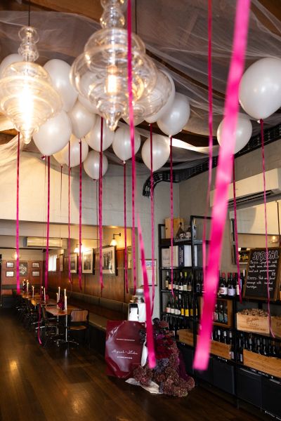 White balloons with pink ribbons decorate a cozy, rustic restaurant interior.