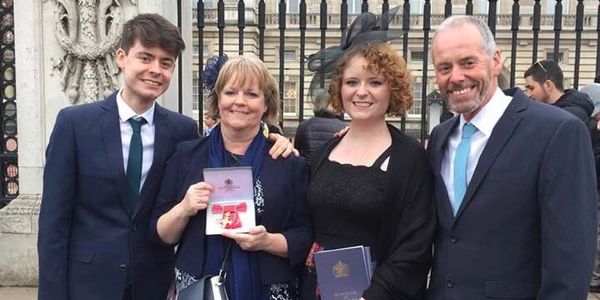 Sam Twiselton holding her OBE with her family outside Buckingham Palace