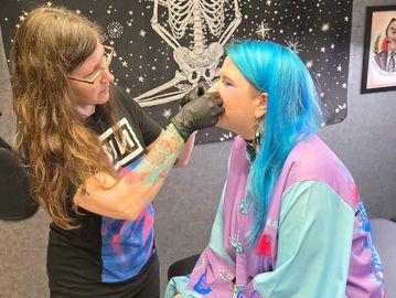 A woman with blue hair getting a piercing.