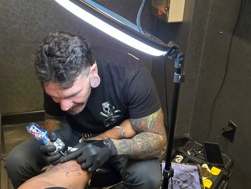 Tattoo artist working on a client's leg under bright light.