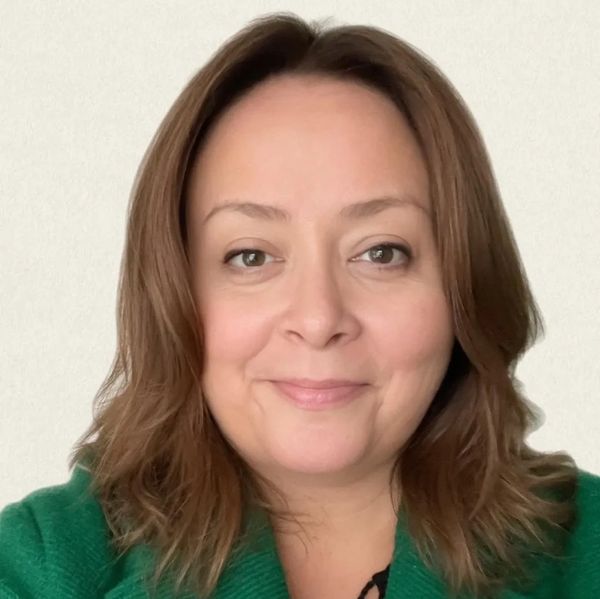 Woman with brown hair wearing a green coat, smiling gently.