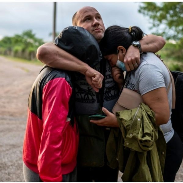 Three people embrace tightly, sharing a moment of comfort and support outdoors.
