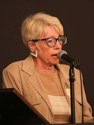 Elderly woman speaking into a microphone at a podium.