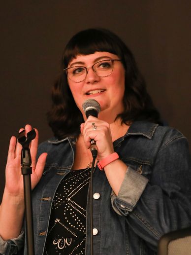 Woman speaking into microphone with expressive hand gesture.
