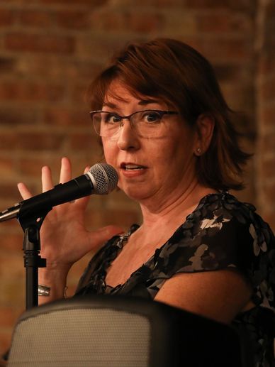 A woman speaking into a microphone with expressive hand gesture.