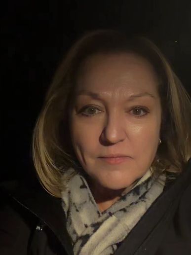 Woman wearing a scarf and jacket looking at the camera in low light.