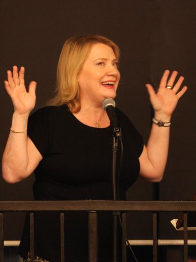 A woman speaking and gesturing enthusiastically behind a microphone.
