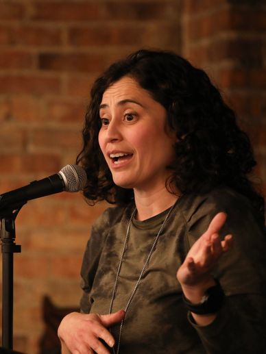 Woman speaking into a microphone with expressive gesture.