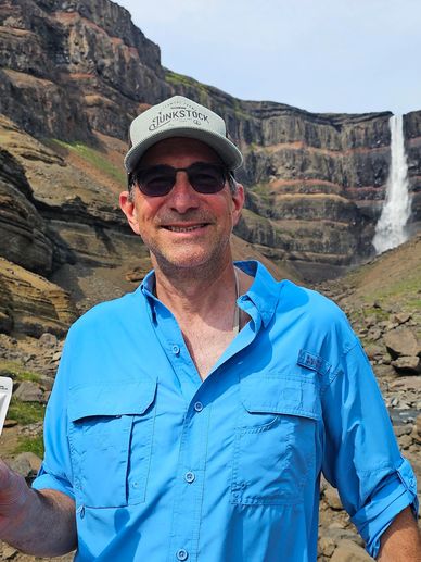 Man in blue shirt and cap with waterfall behind.