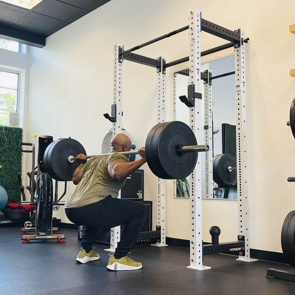 Client performing barbell squat as part of strength training and performance-based physical therapy