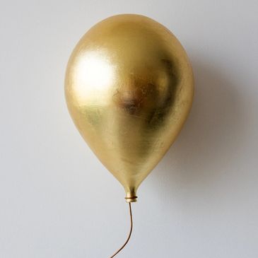 A single gold balloon with a curly string on a plain background.