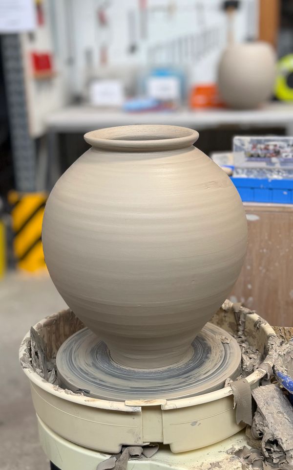 A large, unpainted clay pot on a pottery wheel in a workshop.