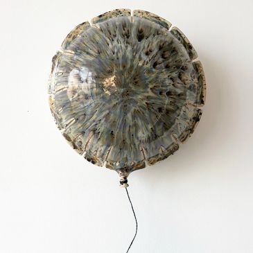 A ceramic balloon sculpture with intricate glaze and a string attached.