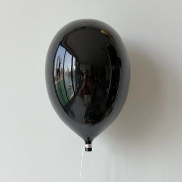 Glossy black balloon with a slim fit design against a white wall.