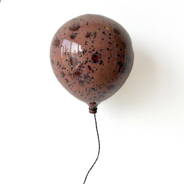 A speckled plum balloon with a thin black string against a white background.