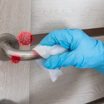 Gloved hand disinfecting a door handle with virus particles visible.