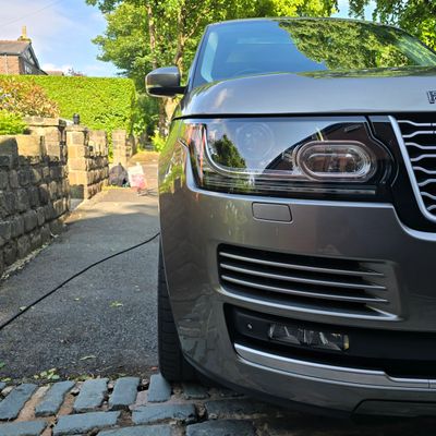 Close-up of a silver Range Rover front headlight and grille in a driveway.