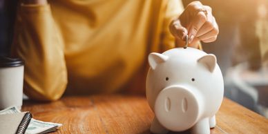 Someone putting money into a pig shaped piggy bank.