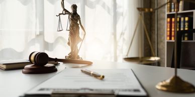 Notebook and pen, gavel, and a statue that symbolizes justice in a professional office.