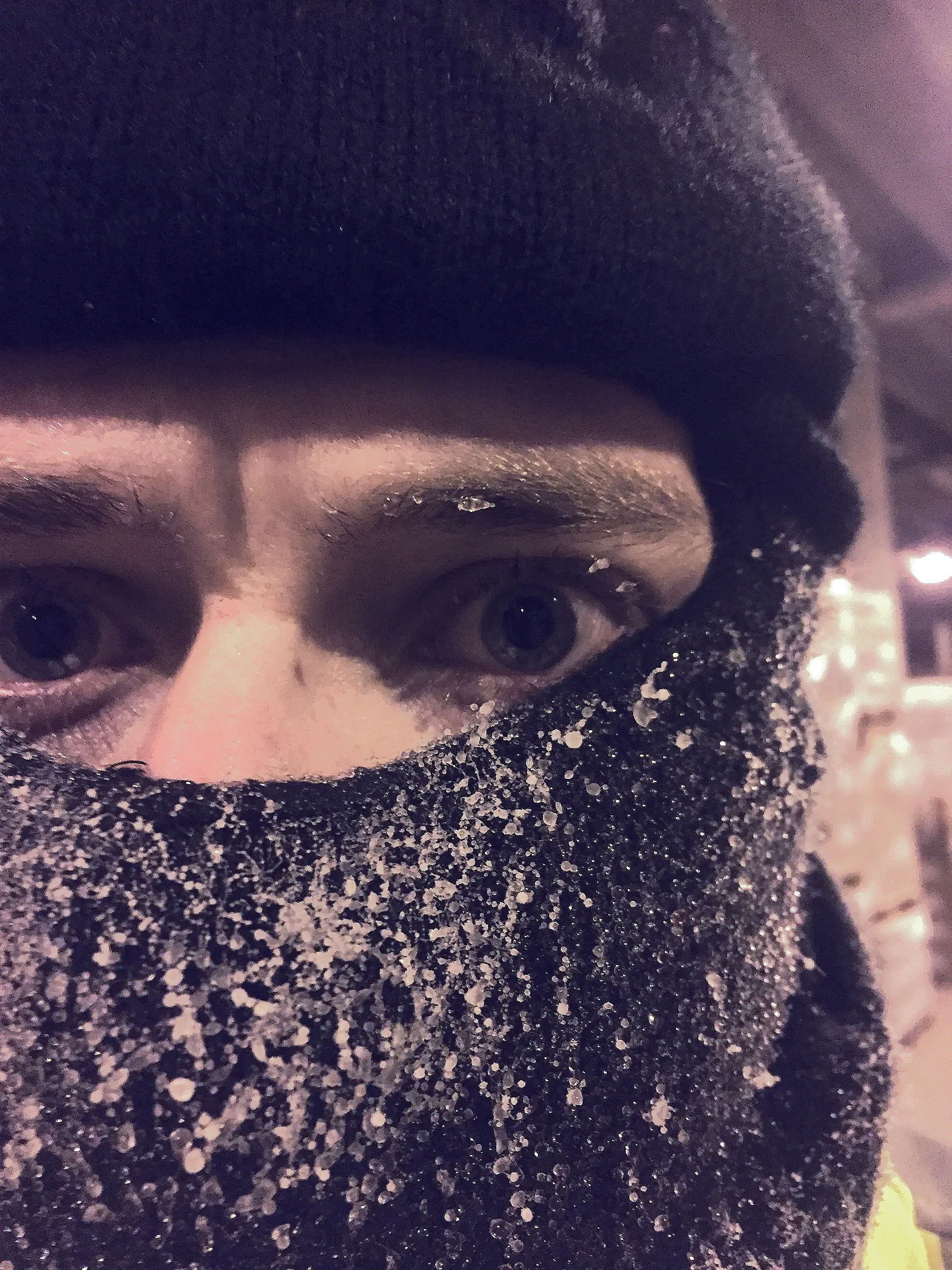 Close-up of a person with icy frost on their black face mask and hat.