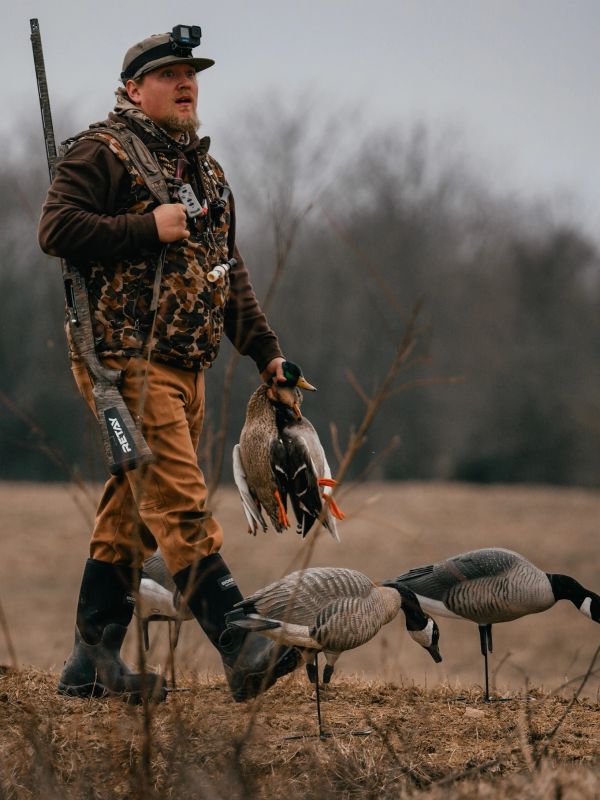 Hunter carrying ducks with a rifle on his shoulder.