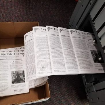 Newspapers titled 'Top of the Hill' being printed and collected.