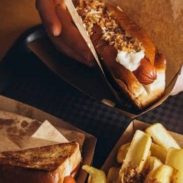 Person holding a loaded hot dog with fries and sandwich nearby.