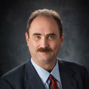 Professional portrait of a man in a suit with a mustache.