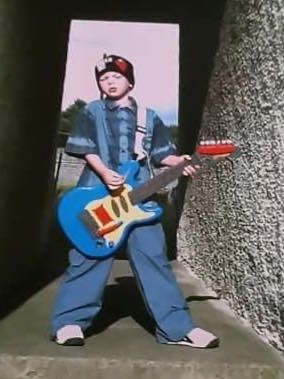 a picture of the author age 5 with a green day beanie, standing like billie joe with a toy guitar.