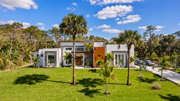 Modern white house with palm trees and a green lawn under a blue sky.