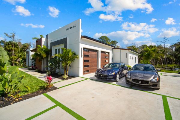 Modern house with two luxury sports cars parked outside on a sunny day.