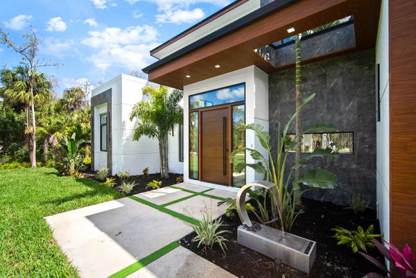 Modern house entrance with glass door and tropical landscaping.