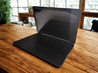 Black HP laptop on a wooden table in a bright room.