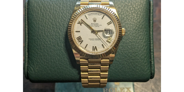 Gold Rolex Day-Date watch on green leather cushion.