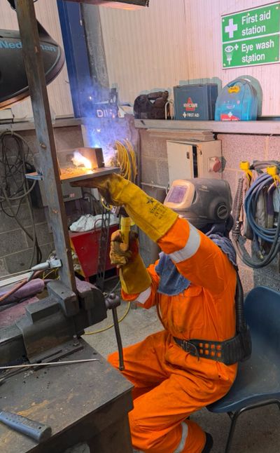 Worker welding metal, wearing protective gear and gloves in a workshop.