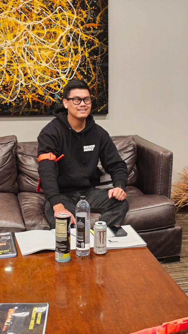 A young man sitting on a brown leather couch with drinks on a wooden table.