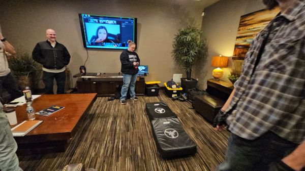 People gathered in a living room with a video call on TV and cornhole boards on the floor.