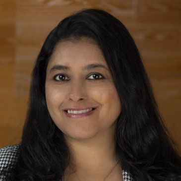 Smiling woman with long black hair against a wooden background.