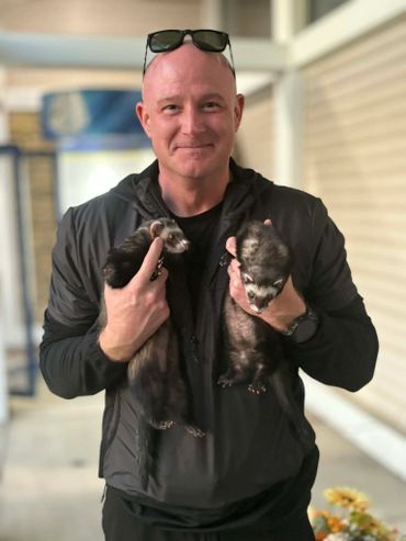 Man holding two ferrets and smiling at the camera.