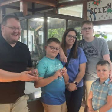 A family of five smiles inside a science exhibit area.
