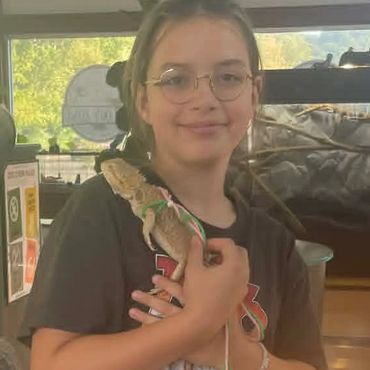 Young girl holding a bearded dragon lizard indoors.