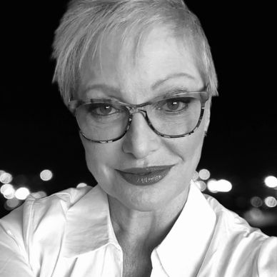 Headshot of Miranda Armstadt smiling wearing eyeglasses and white collared blouse with city backdrop