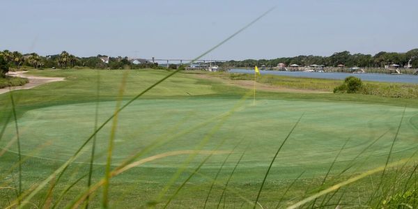 Golf course green with a flag near water.