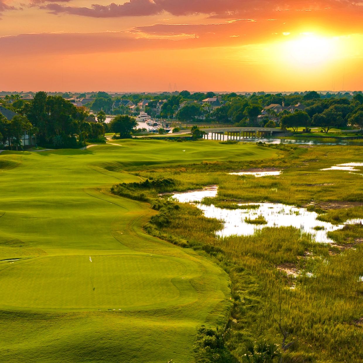 Golf course at sunset with vibrant orange sky.