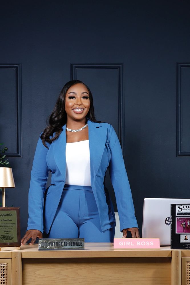 Confident woman in a blue suit stands behind a stylish desk with inspirational plaques.