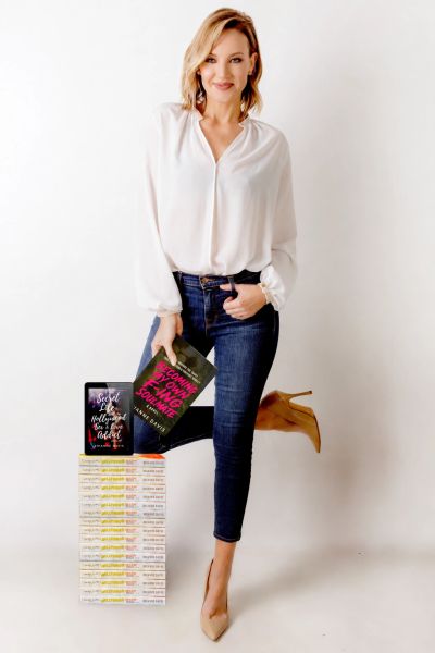 Woman holding a book with a stack of books beside her.