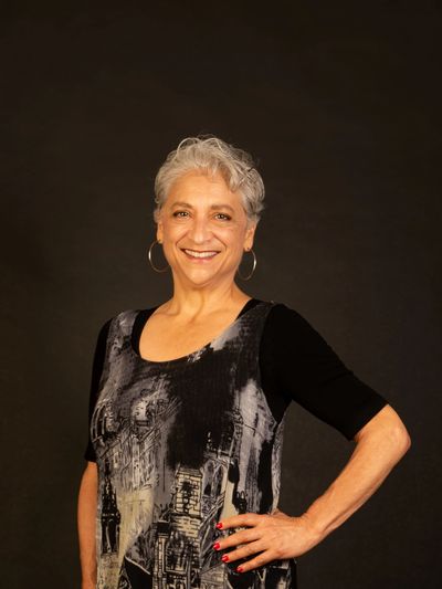 Confident older woman smiling against a dark background.