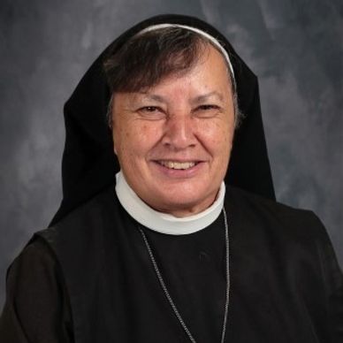 Smiling nun in traditional habit with gray background.